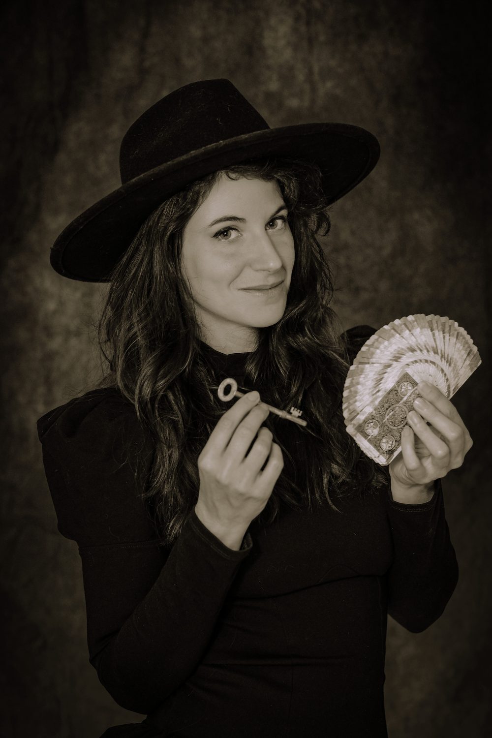 Portrait de Mira Jane au chapeau noir, tenant une clé ancienne et un éventail de cartes de magie
